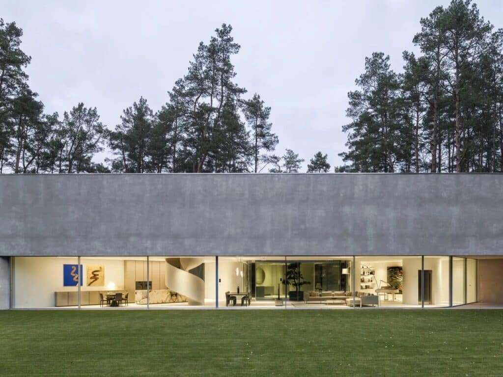 Evening wide shot of Trim House with interior lights glowing through a continuous horizontal glass wall.