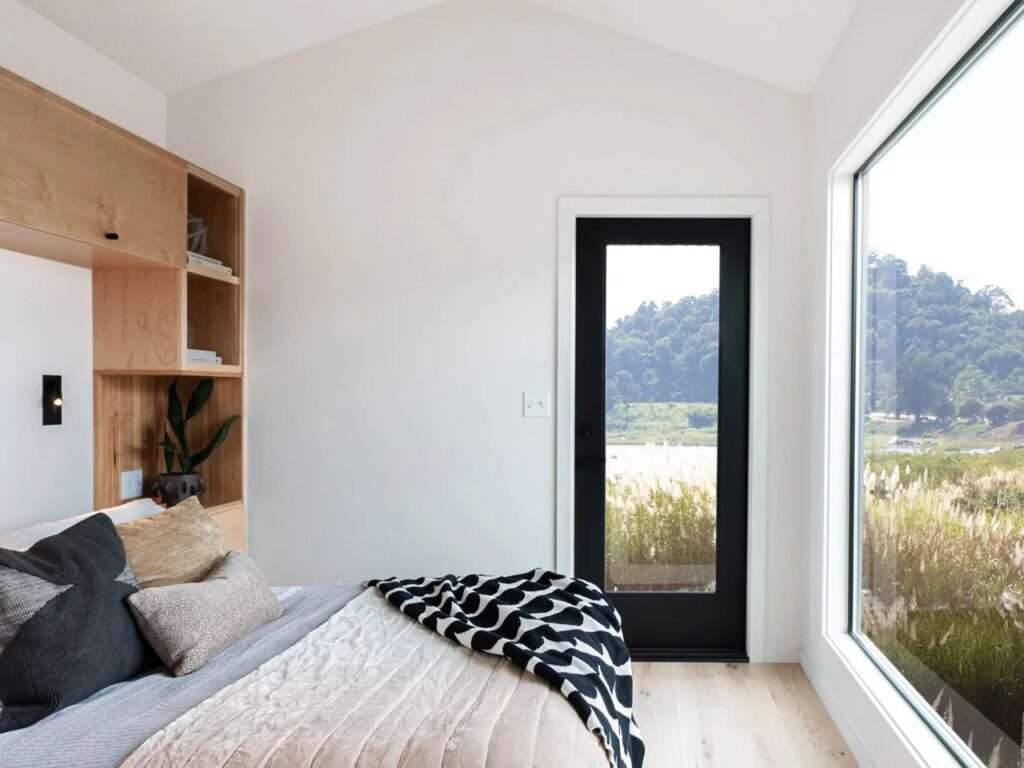 Minimalist bedroom in a tiny home with a large picture window overlooking a field.