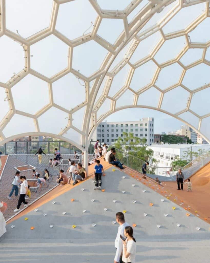 Children playing on the climbing slopes of the Yongping Warehouse rooftop under the large hexagonal canopy.