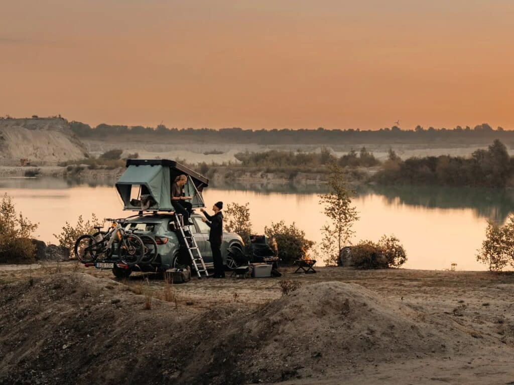 Wide shot of a camping setup by a lake with a Thule Widesky tent deployed on an SUV during twilight.