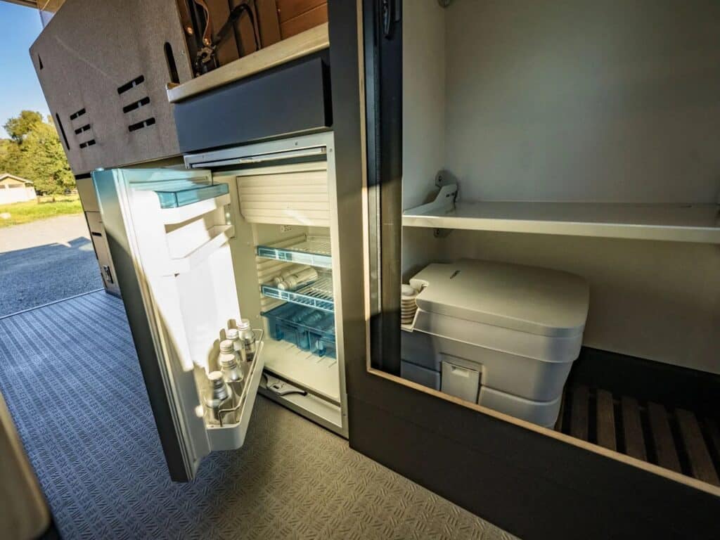 Detail of the internal storage unit featuring a small refrigerator and a portable toilet in a dedicated compartment.