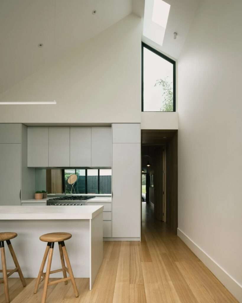 Modern white kitchen with a minimalist island bench and a hallway leading toward the front of the heritage house.