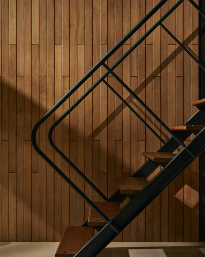 Minimalist interior staircase with black metal handrails against a vertical wood slat wall in an Eames house.