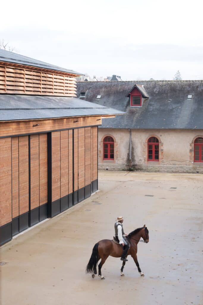 A rider on horseback in the courtyard of Haras National d'Hennebont with the new timber performance hall in the background.