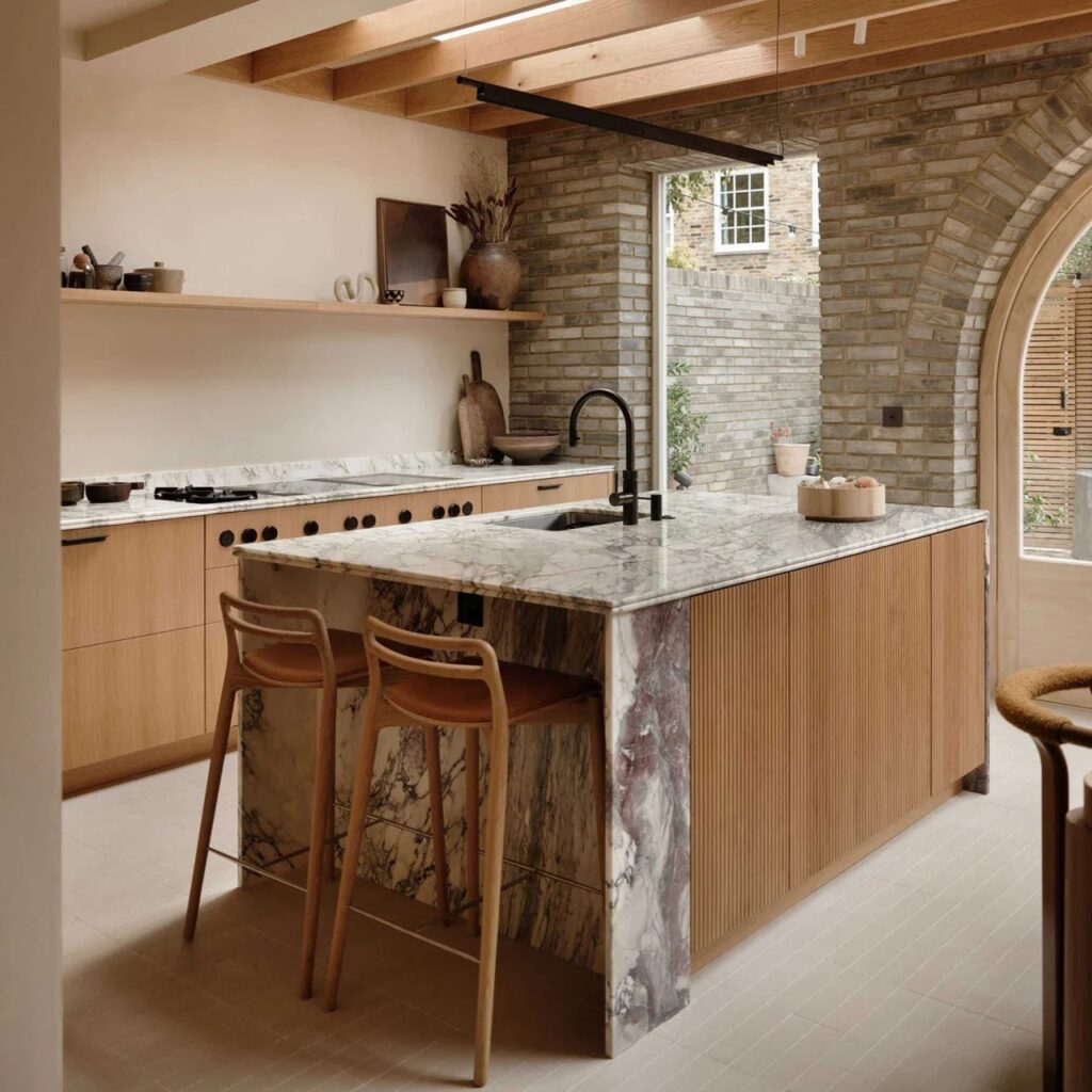 Modern kitchen island with white veined marble countertop and fluted wooden base in a minimalist interior.