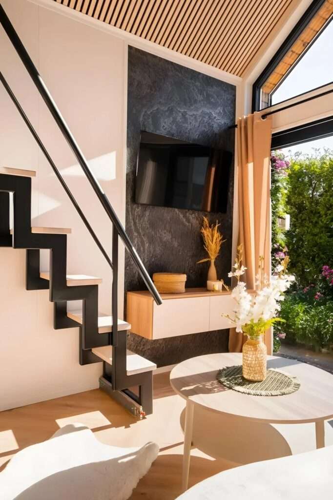 Modern black metal staircase leading to a loft, next to a living area with a stone-textured TV wall.