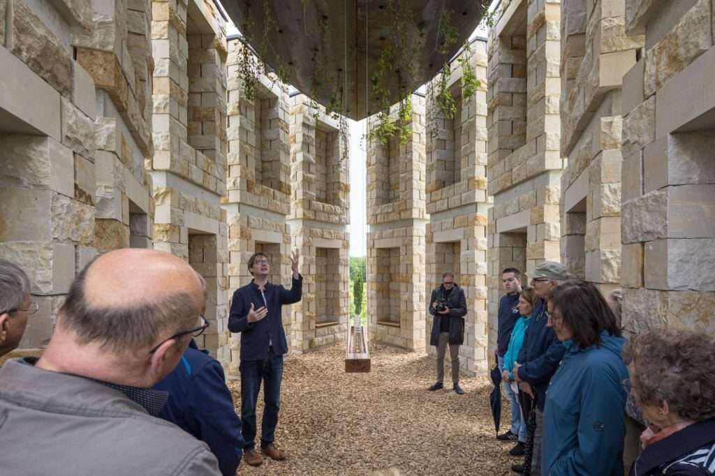 A group of visitors listening to a presentation inside the Open Chapel under a vegetated roof structure.