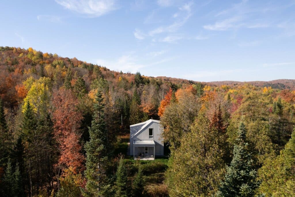Distant aerial view of Scotch Chalet nestled on a plateau within a vast, colorful forest landscape under a blue sky.