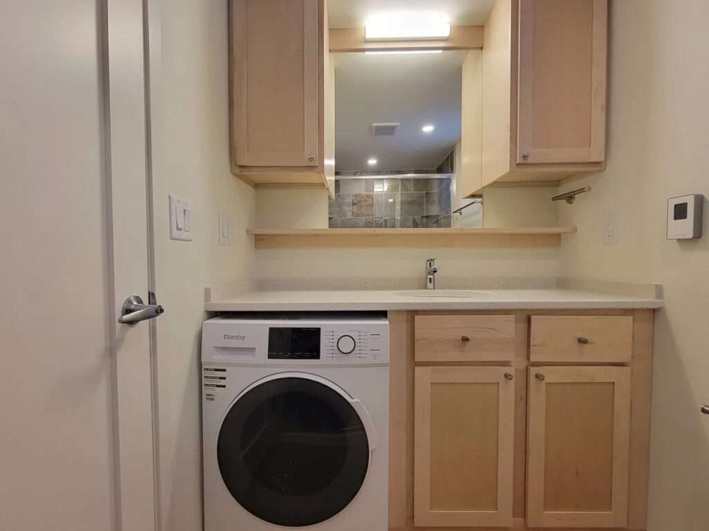 Functional bathroom vanity in Shoreline House including a built-in washing machine and overhead storage.