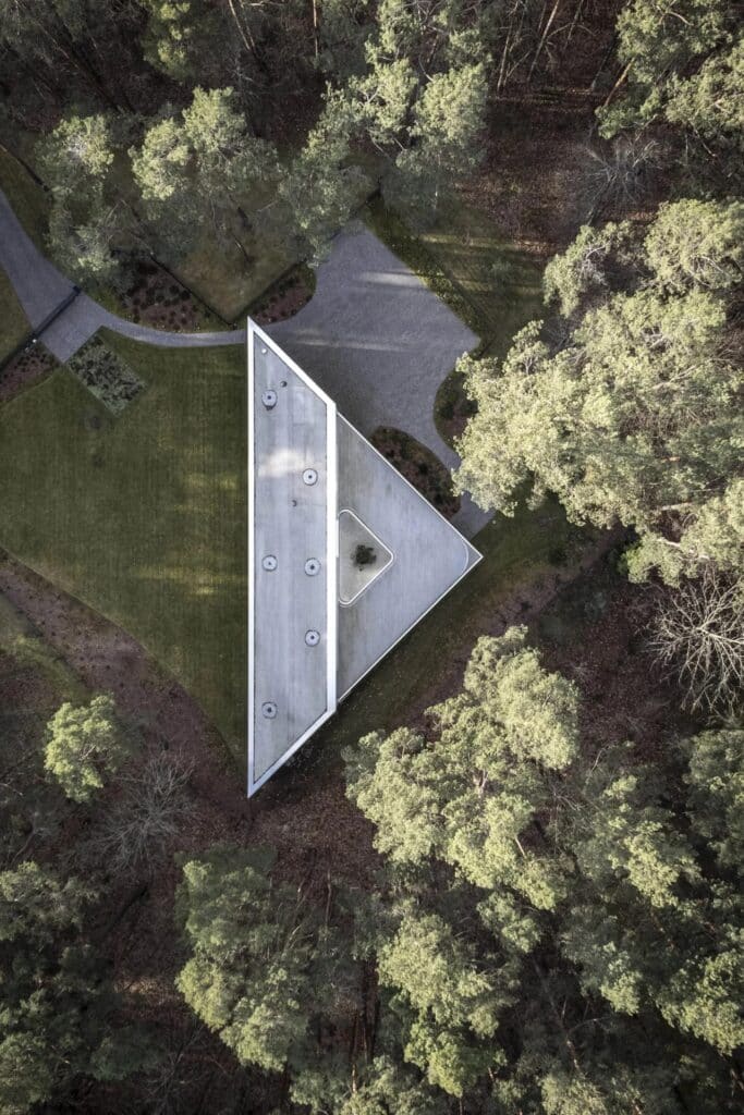 Aerial top-down view of the triangular roof of Trim House surrounded by a dense pine forest in Vilnius.