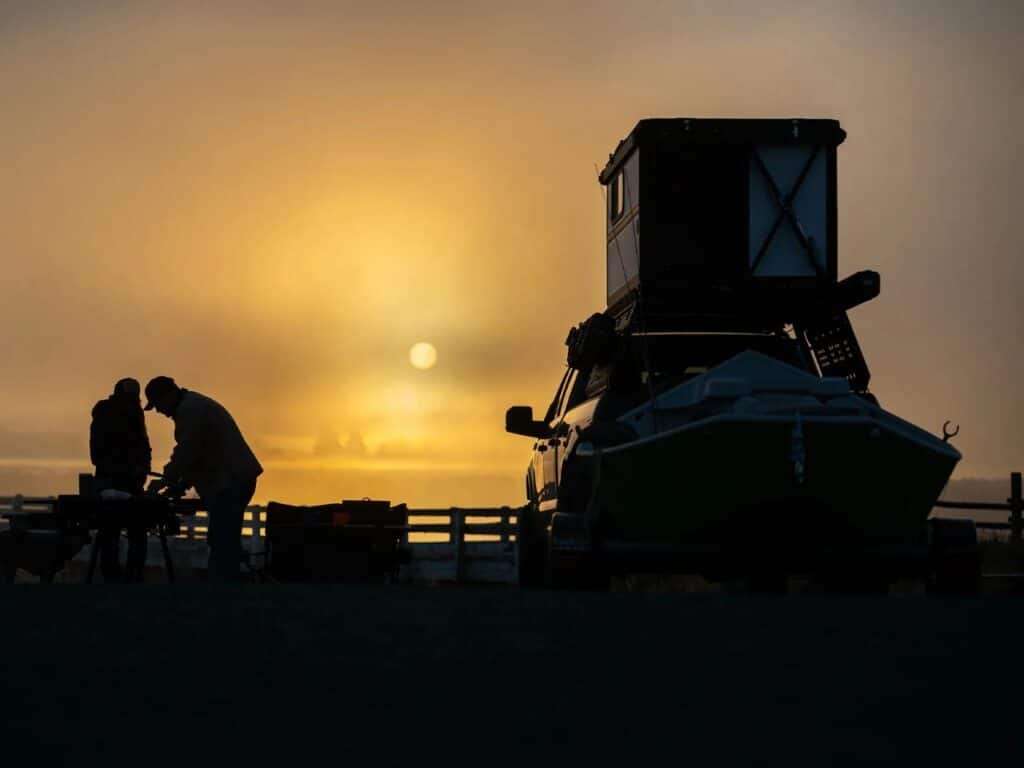 Silhouette of an Altus-equipped truck and campers against a golden sunrise.