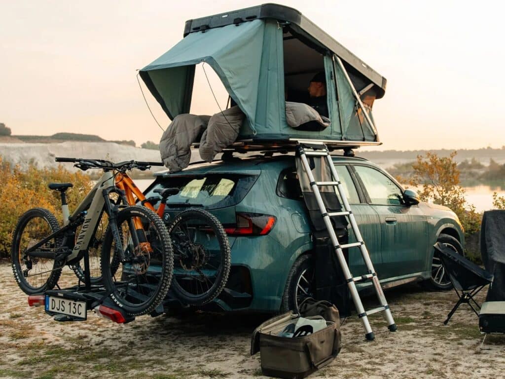 Side view of the Thule Widesky tent deployed on a green BMW SUV with bikes mounted on the rear.