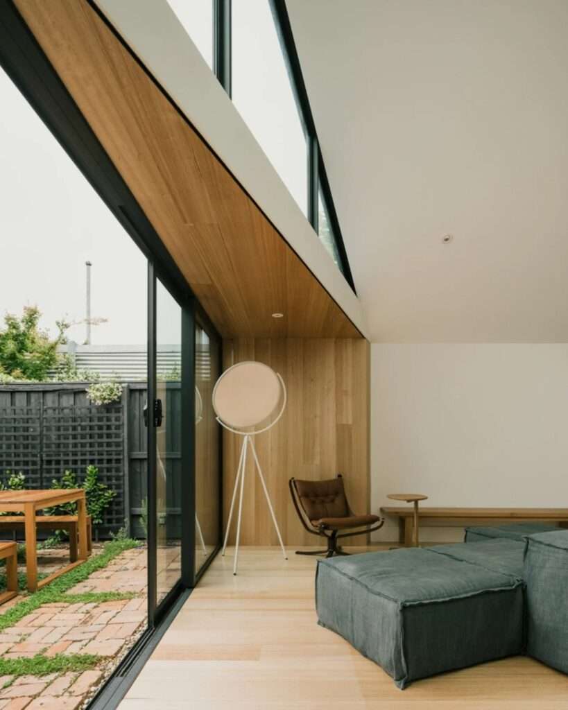 Close-up of timber-lined interior walls and a sliding glass door leading to a sunlit brick courtyard with outdoor furniture.