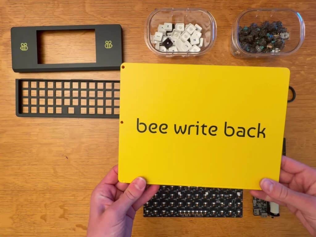 Hands holding the yellow backplate of the Bee Write Back with the project name engraved.