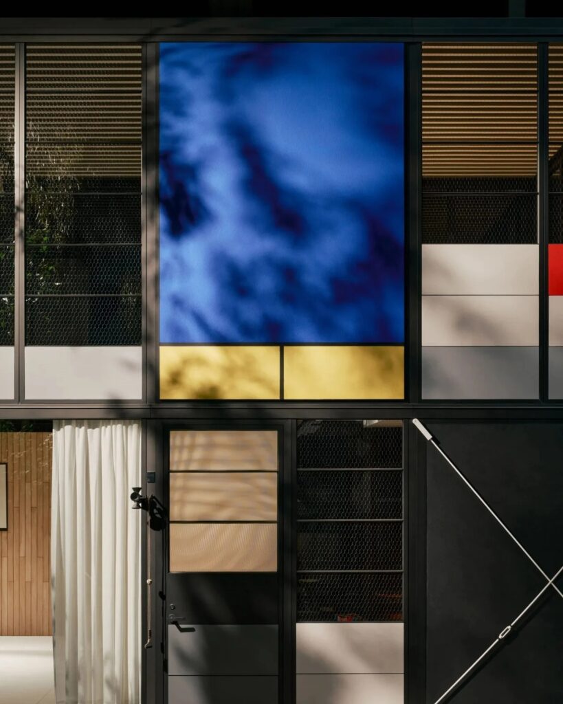 Exterior facade of Eames Pavilion showing blue and yellow panels with tree shadows cast on glass.