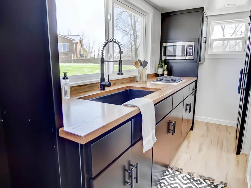 Close-up of the Espresso tiny house kitchen featuring a black granite undermount sink and solid wood countertops.