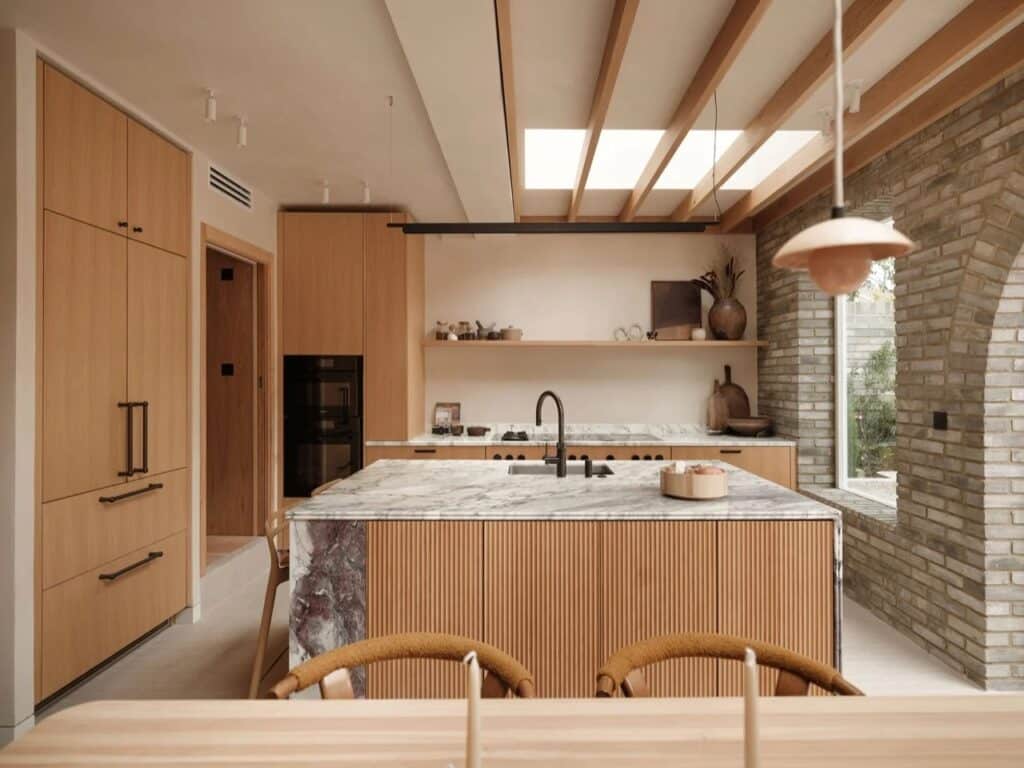 Contemporary kitchen in Islington House featuring an oak wood island with marble top, exposed Douglas fir beams, and a skylight.