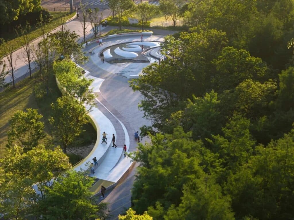 Curved white seating steps following the riverbank with a musical fountain area in a park setting at sunset.