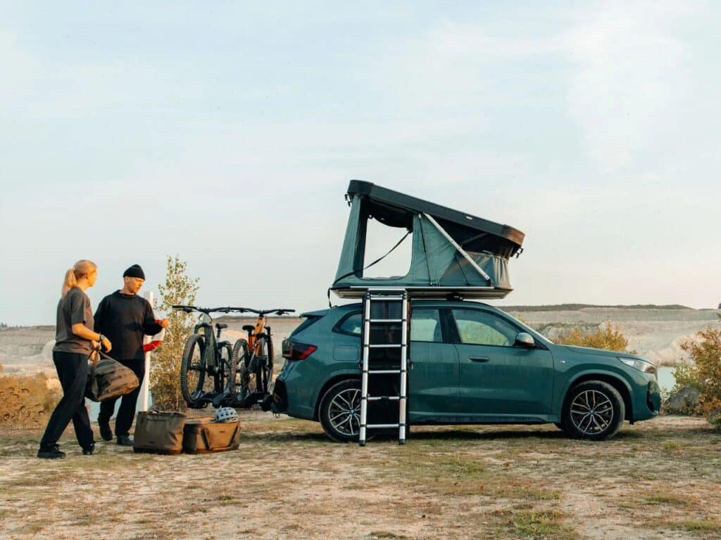 A couple preparing for a trip next to an SUV equipped with a Thule Widesky tent and bike rack.