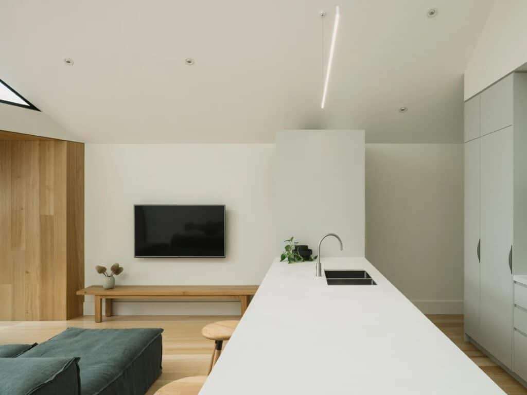 Minimalist white kitchen island with a sleek faucet and a wall-mounted TV in a bright, open-plan living area.