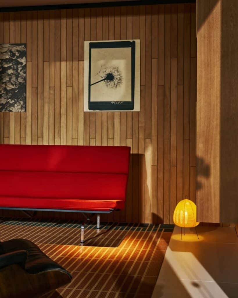 Interior of Eames Pavilion with a red sofa, wood walls, and a warm Akari-style floor lamp.