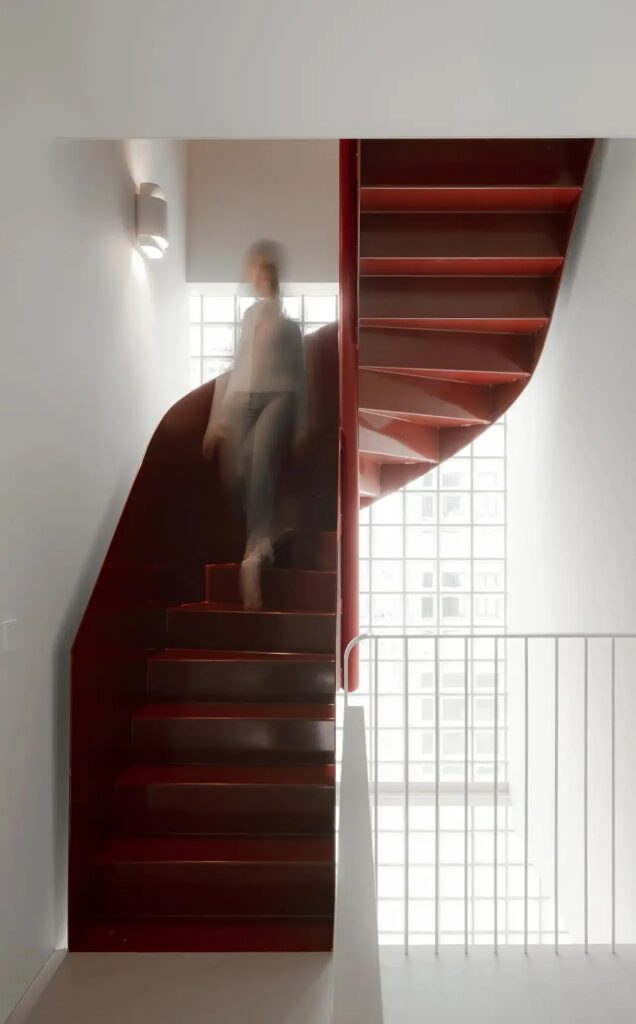 A striking red spiral staircase inside the Light House, set against a background of translucent glass blocks.