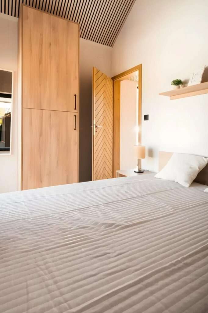 Minimalist bedroom with a tall wooden wardrobe and a custom chevron-patterned wooden door.