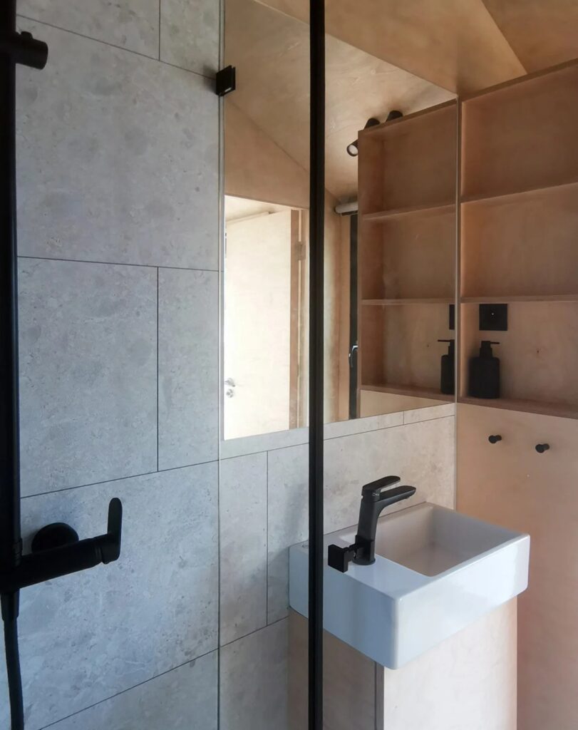 Modern bathroom in the Shoji House with stone-patterned tiles, a white sink, and birch wood storage.