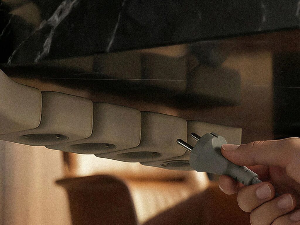 Hand plugging a grey power cord into the bottom outlets of the Edge system under a desk.