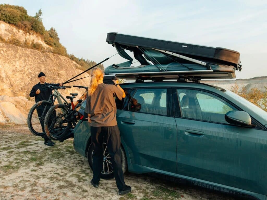 Two people manually adjusting the struts of the Thule Widesky hardshell tent during deployment.