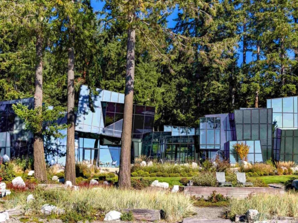 F-House seen from the waterfront, showing the multi-faceted glass volumes integrated into the wooded shoreline.