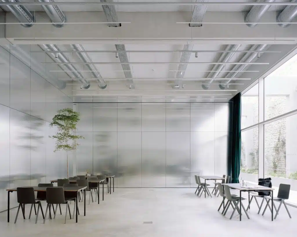 Minimalist workspace in Maison FLOW featuring full-height reflective aluminum panels and exposed ceiling technical systems.