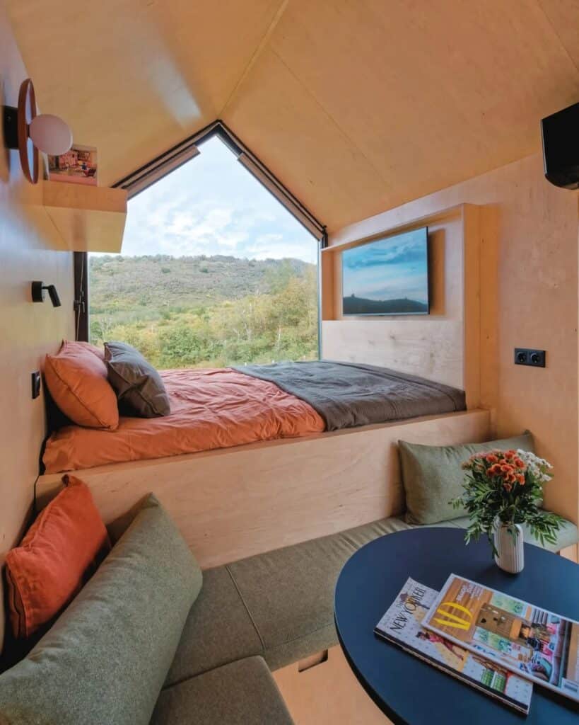Close-up of the interior living and sleeping area in NestOff cabin with birch wood walls, green cushions, and a TV.