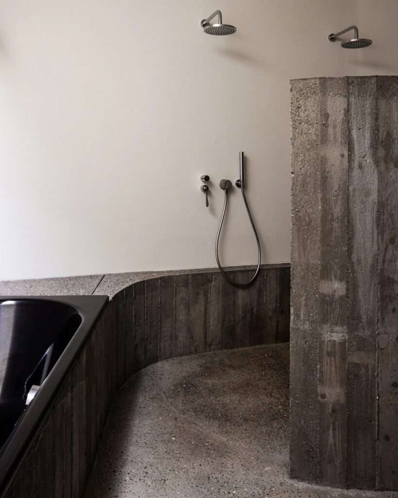 Minimalist bathroom with curved concrete walls, exposed aggregate flooring, and modern shower fixtures.