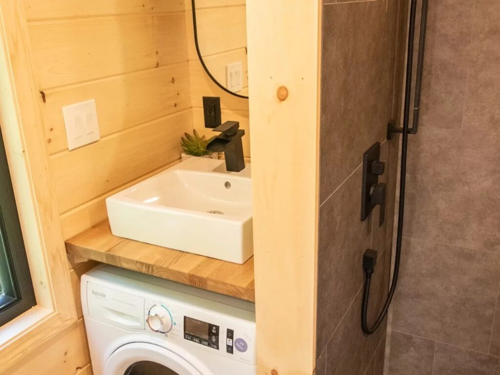 Compact bathroom in Scandi Inn with a vessel sink, wooden counter, and an under-counter washing machine.