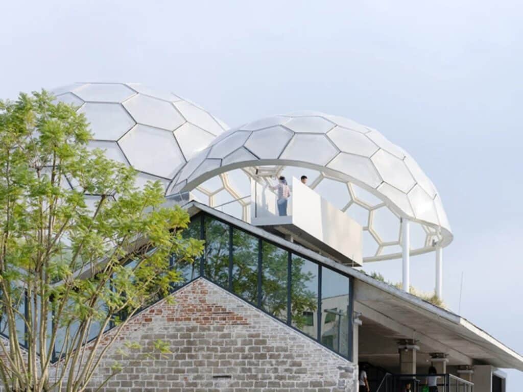 Low-angle exterior shot of Yongping Warehouse renovation featuring original brick walls, modern glass gables, and lightweight hexagonal domes.