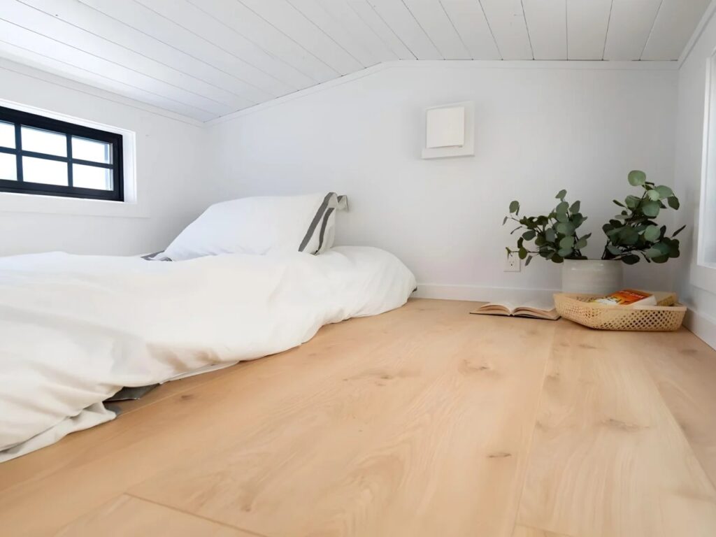 Minimalist loft bed setup in Harmony tiny home with natural lighting and white walls.