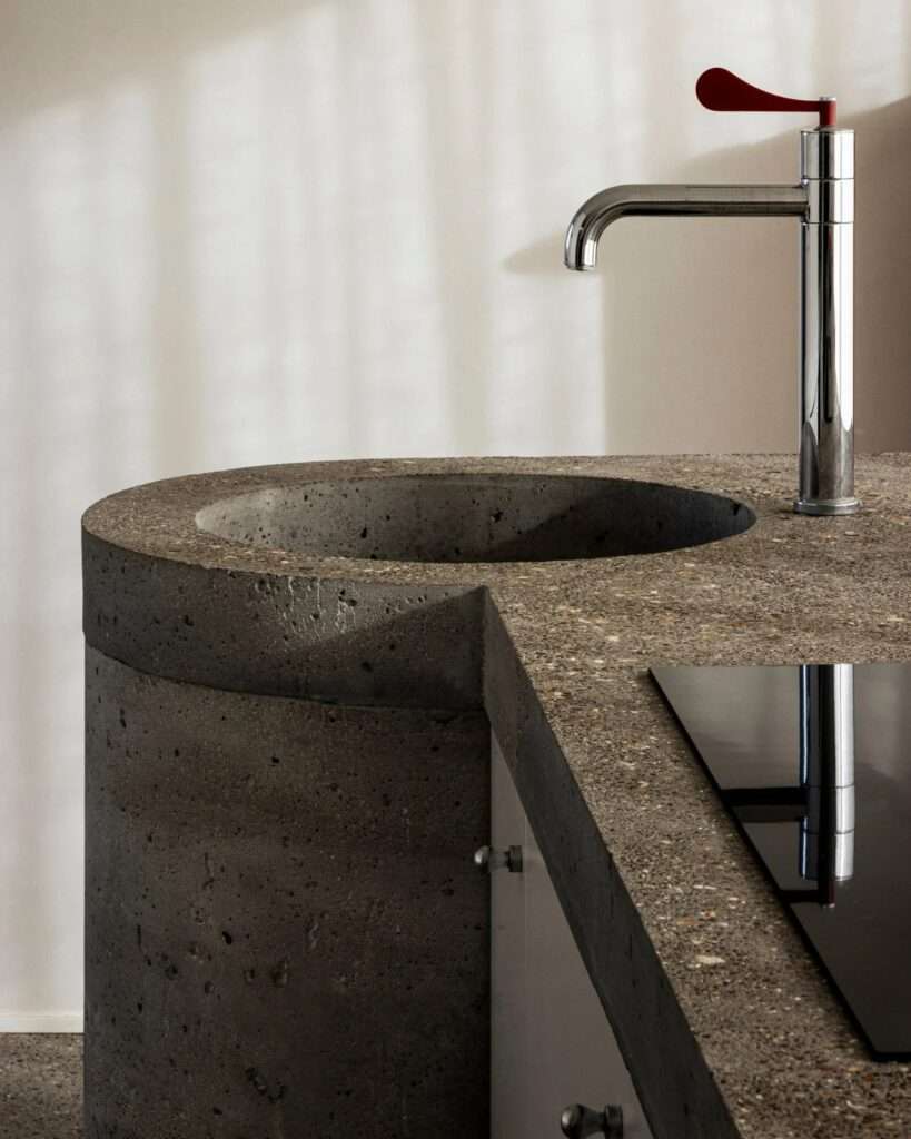 Close-up of a custom raw concrete kitchen sink and countertop with a modern chrome faucet at Villa Nouvelle Vague.
