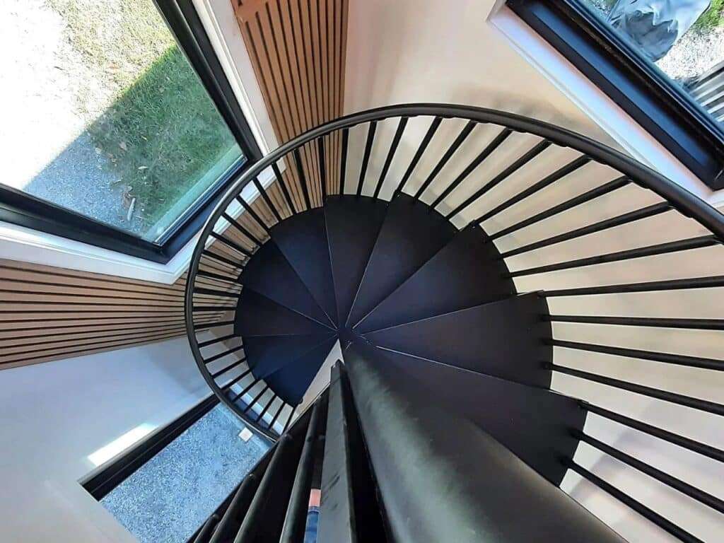 Top-down view of a black spiral staircase inside a modern container home with wood-slat wall panels.