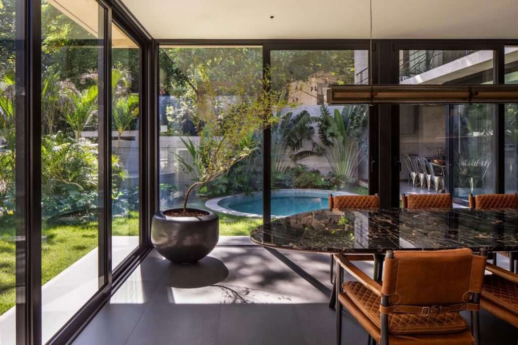 Interior dining room with a black marble table looking out through floor-to-ceiling glass walls toward the pool.