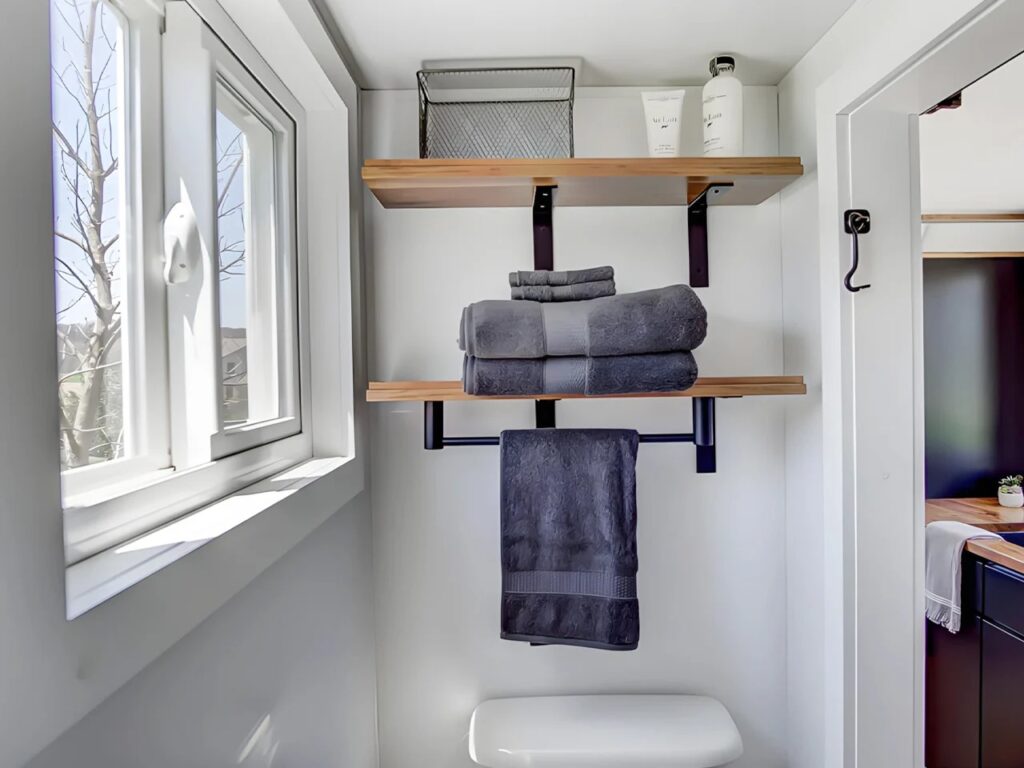 Bathroom interior of the Espresso tiny house with open wooden shelves and black towel racks.