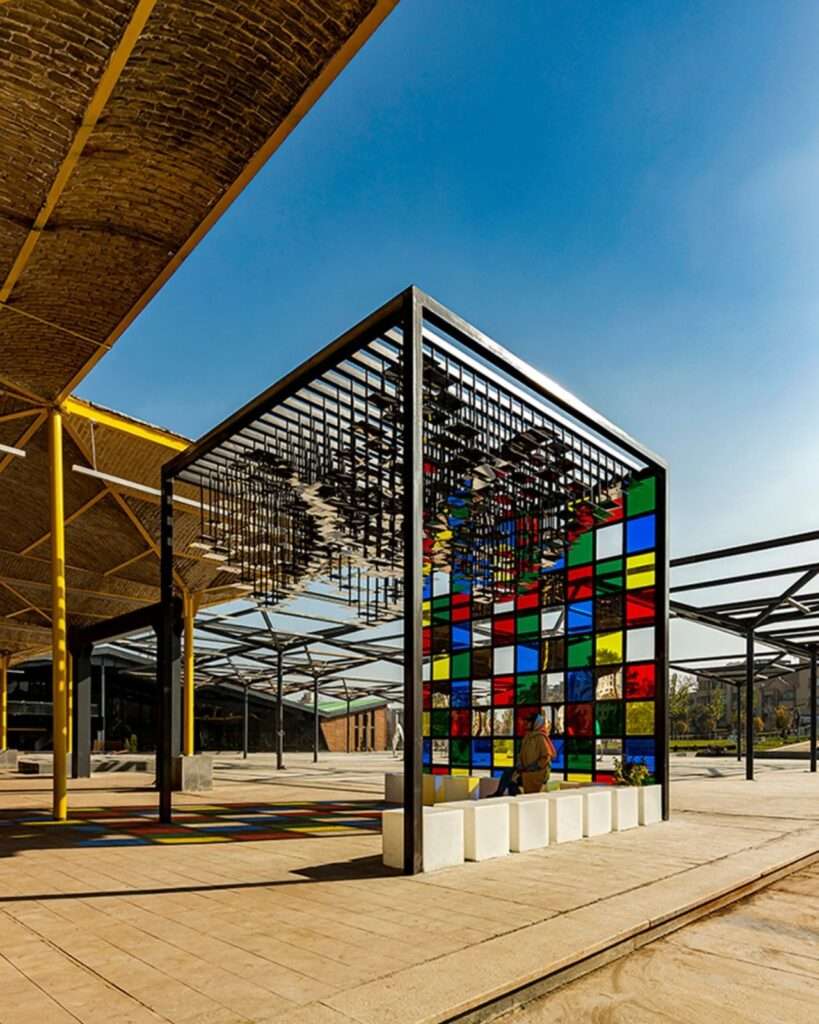 Perspective view showing the contrast between the pavilion's reflective ceiling and the yellow structural beams of the industrial hall.