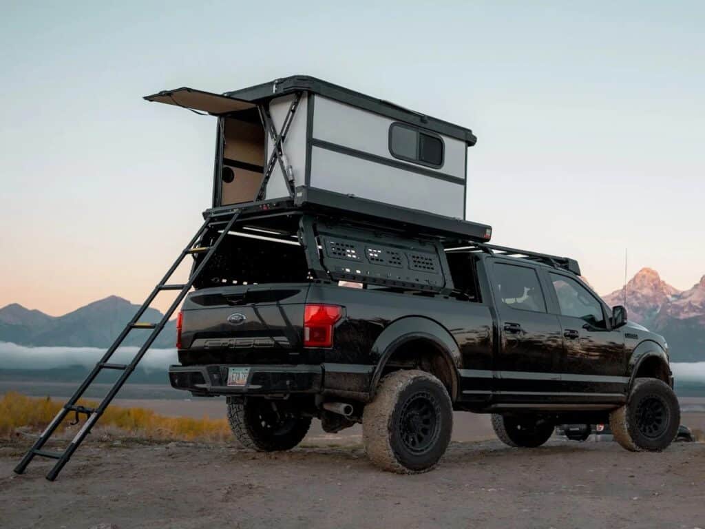 Rear view of a black Ford F-150 with an Altus hardwall rooftop cabin fully deployed and an access ladder.