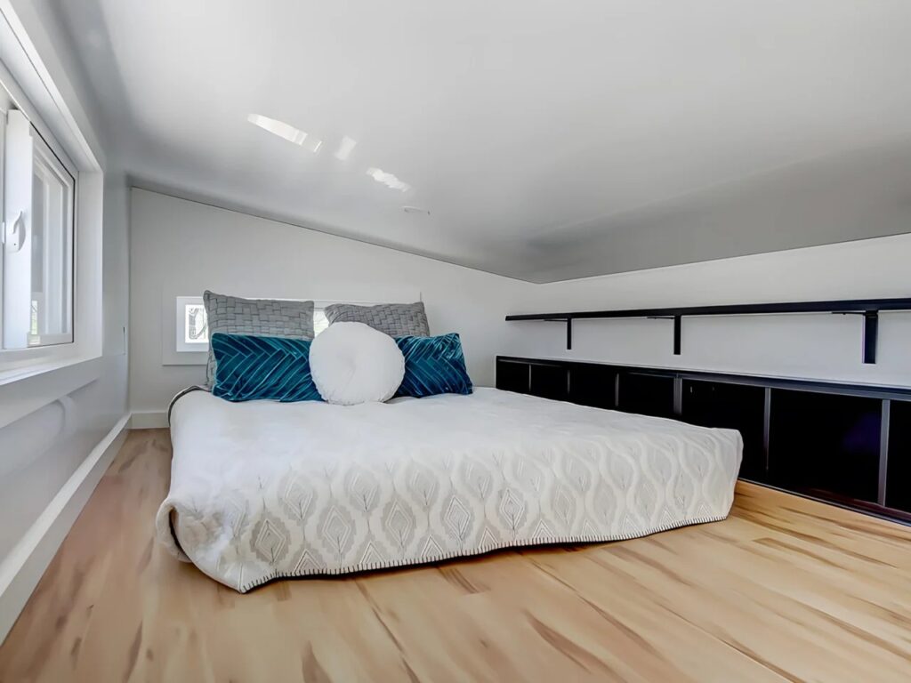 Sleeping loft in the Espresso tiny house with a queen-size bed and built-in black storage cubbies.