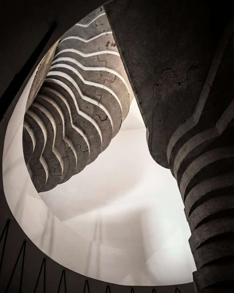 Dramatic low-angle view of a spiraling raw concrete staircase within Villa Nouvelle Vague.