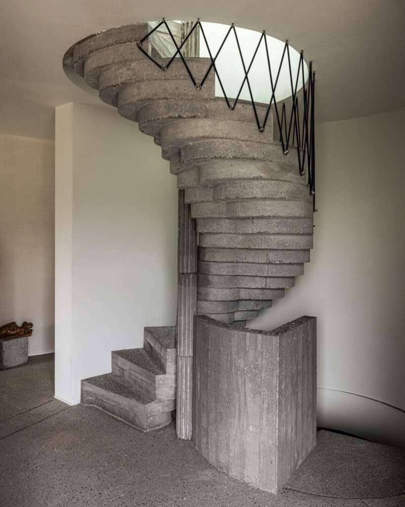 Full view of a spiral concrete staircase with minimalist black metal railings in a white-walled interior.
