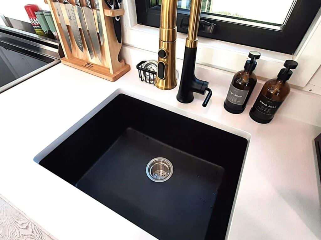 Modern black kitchen sink with a gold designer faucet and wooden knife block at Fairmont Villa.