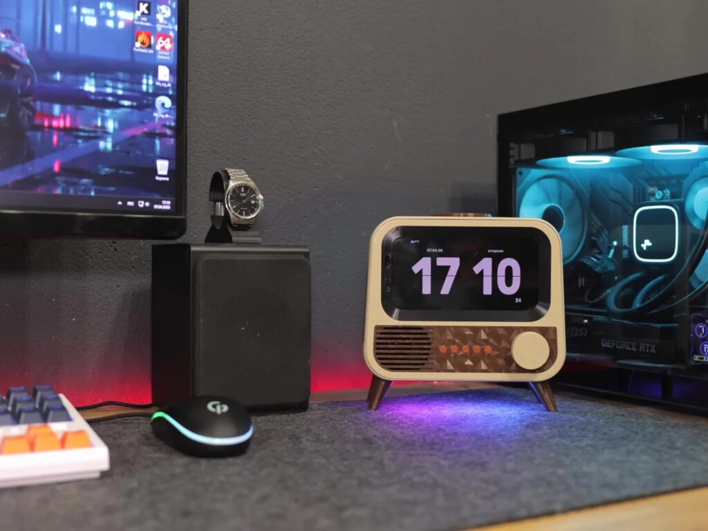 The completed retro-style smart speaker integrated into a modern gaming desk setup next to a PC with blue LED lighting.