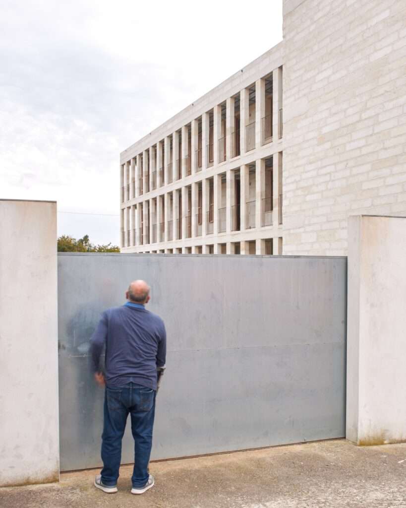 A person standing before the large metal entrance gate of the Santa Margalida social housing project, emphasizing the building's scale.