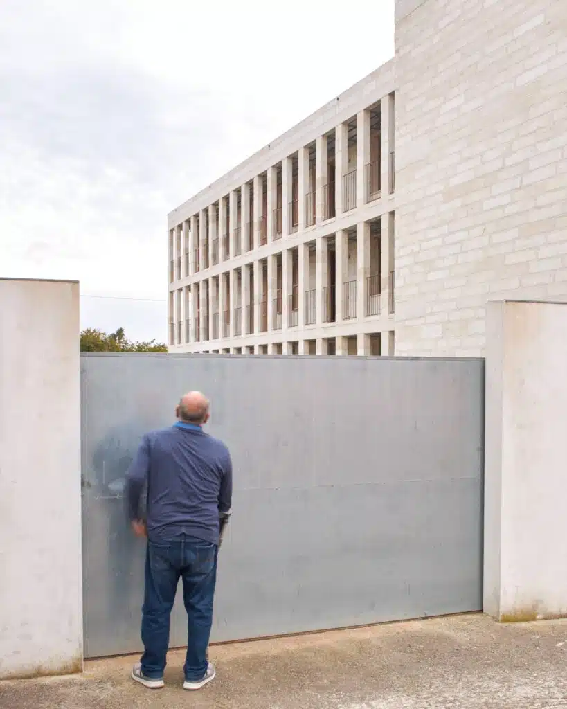 A person standing before the large metal entrance gate of the Santa Margalida social housing project, emphasizing the building's scale.
